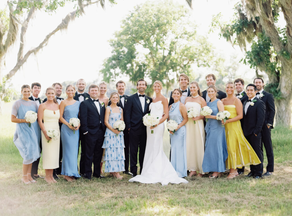 Bridal party group photo under live oak trees and spanish moss. Bridesmaids in mix-matched yellow and blue dresses with different patterns. 