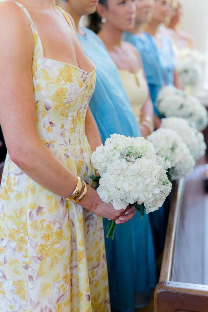 Bridesmaids stand and hold their all white flowers in the pew. Beaufort church wedding ceremony. 