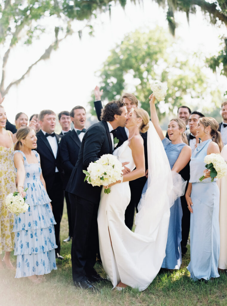 Bridal party celebrates as bride and groom kiss. Wedding film photographer. 