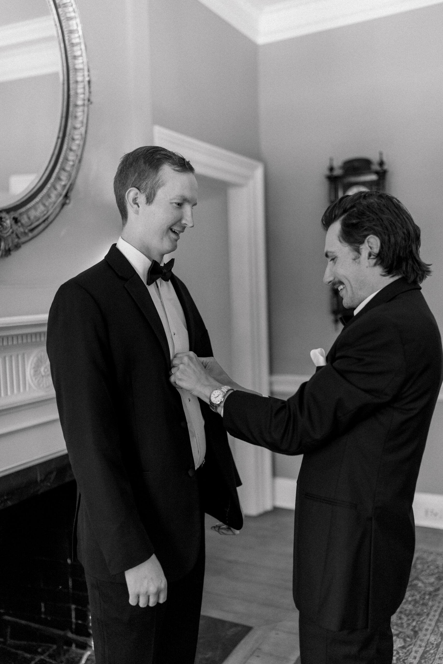 Best man fixes a button on the groom. This photo is black and white.