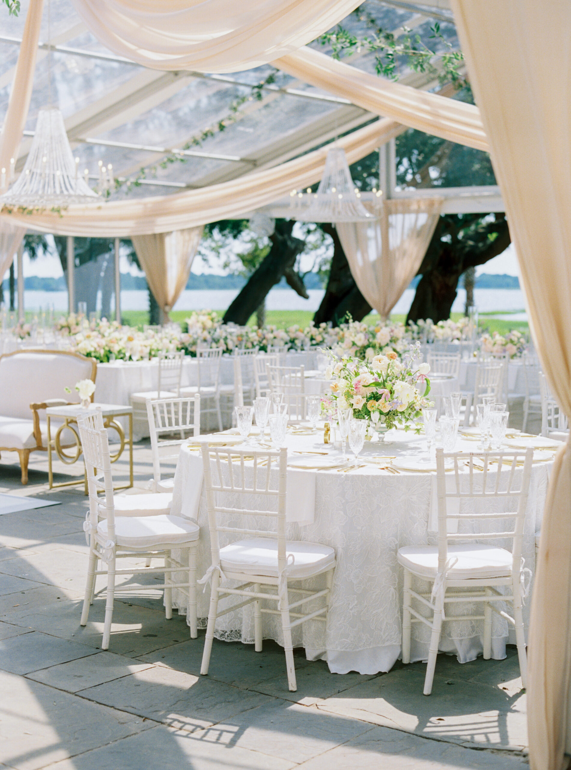 Colorful spring flowers with tan draping and white chandeliers at outdoor wedding reception in Charleston. 