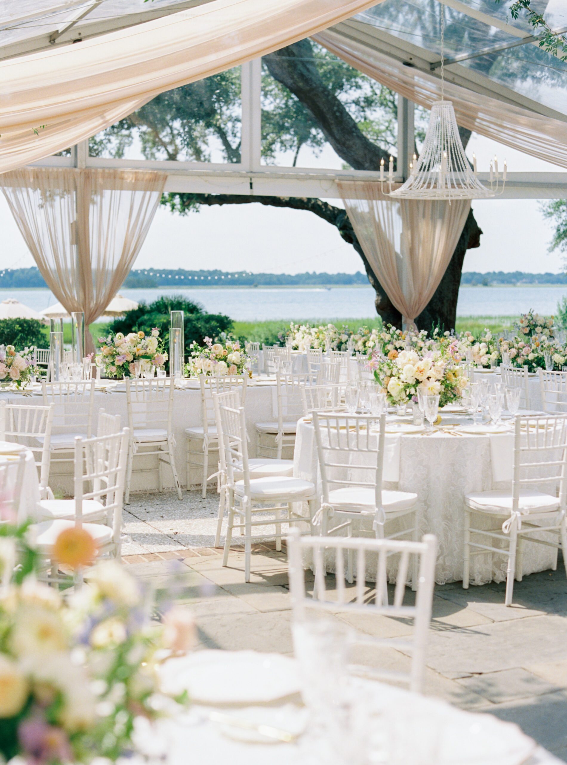 Outdoor wedding reception under clear tent at Lowndes Grove. Tan draping and white chandelier. 