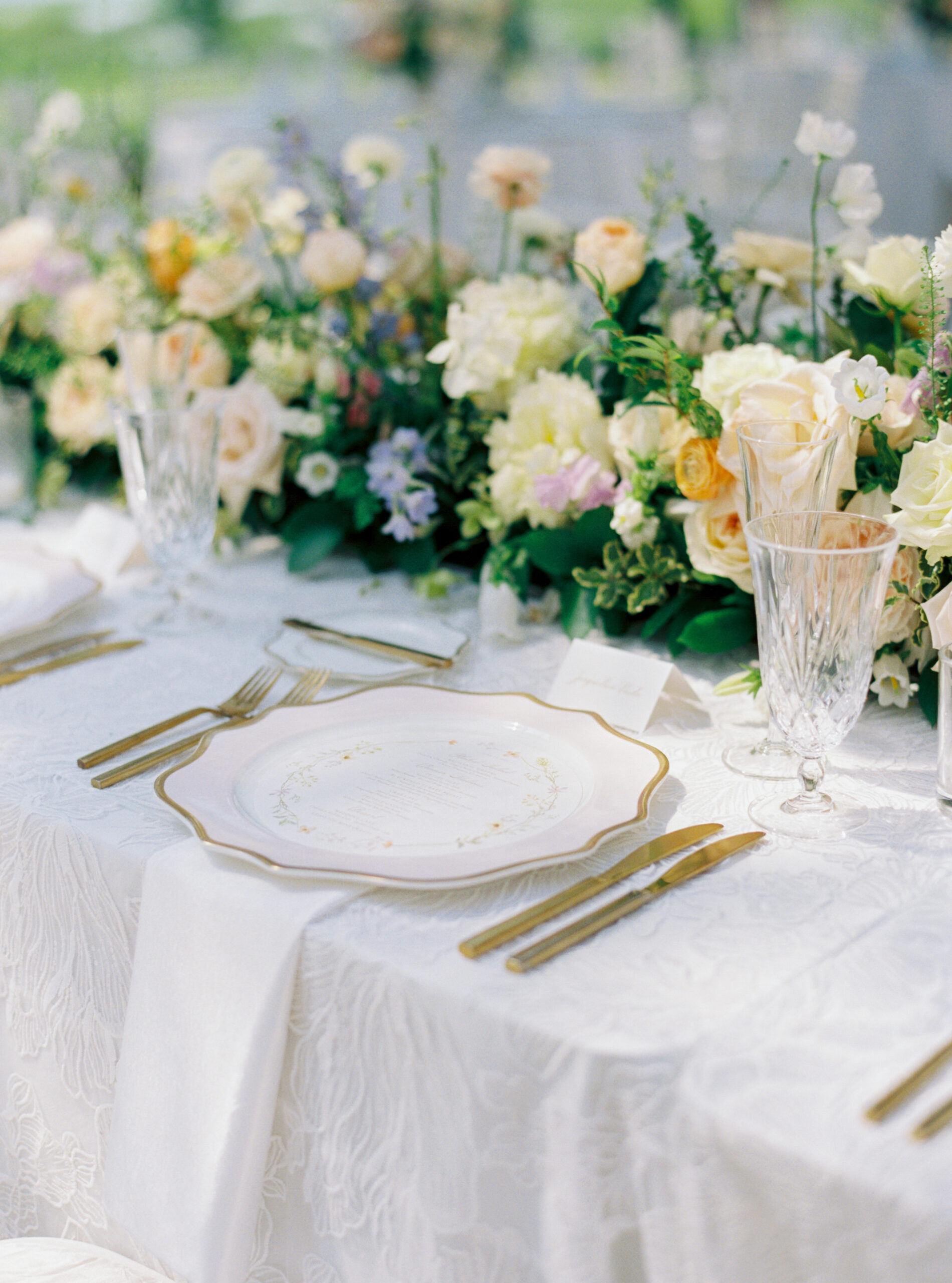 Clear crystal goblets and champagne flutes. Pink and white chargers with a gold rim. Gold forks and knives. Floral patterned white table cloth. Lowndes Grove wedding.