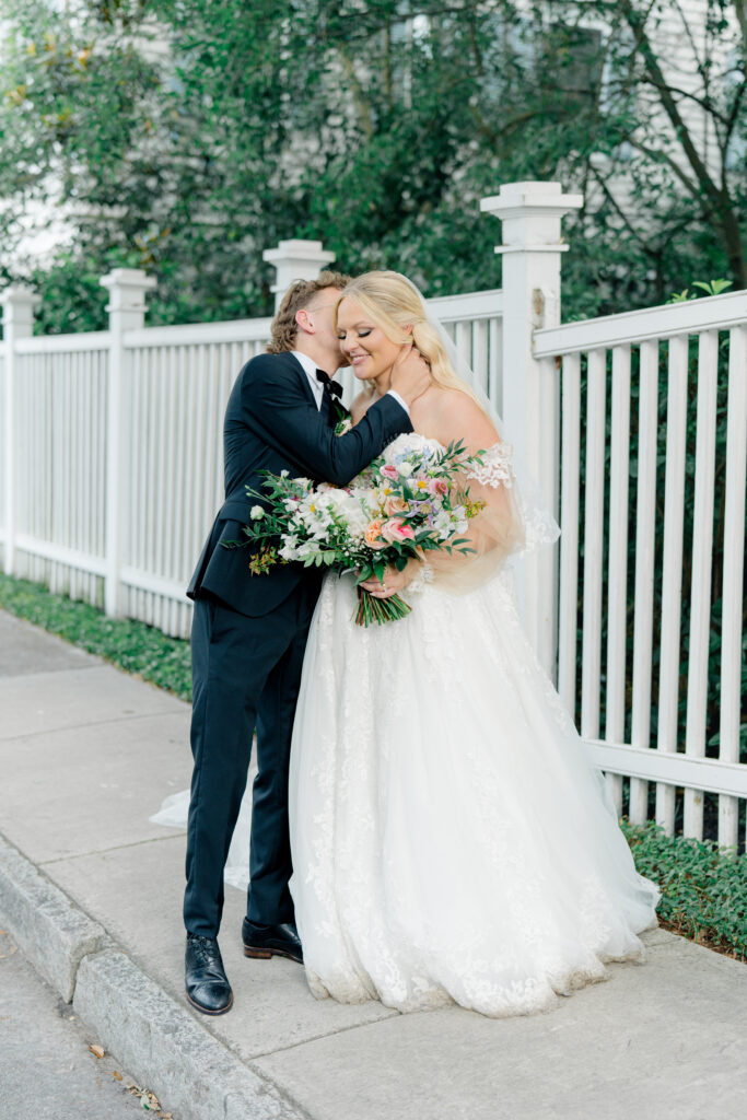 Groom holds brides neck and kisses her cheek. 