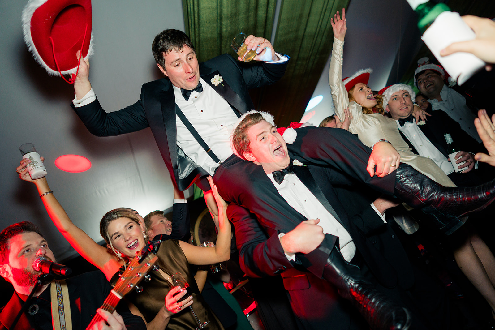 Groom gets on groomsmans shoulder and rides like a bull with santa cowboy hat in one hand and glass in another. 