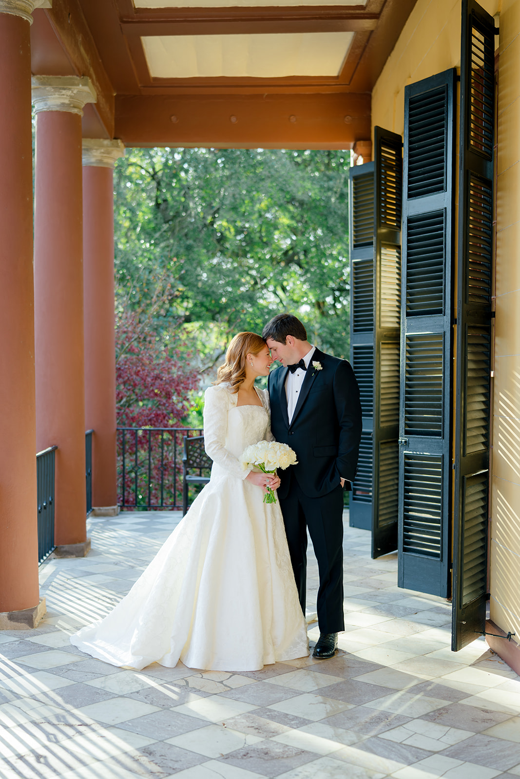Hampton Preston wedding portrait. Bride and groom leaning into each other. Red columns. Checkerboard marble floor.