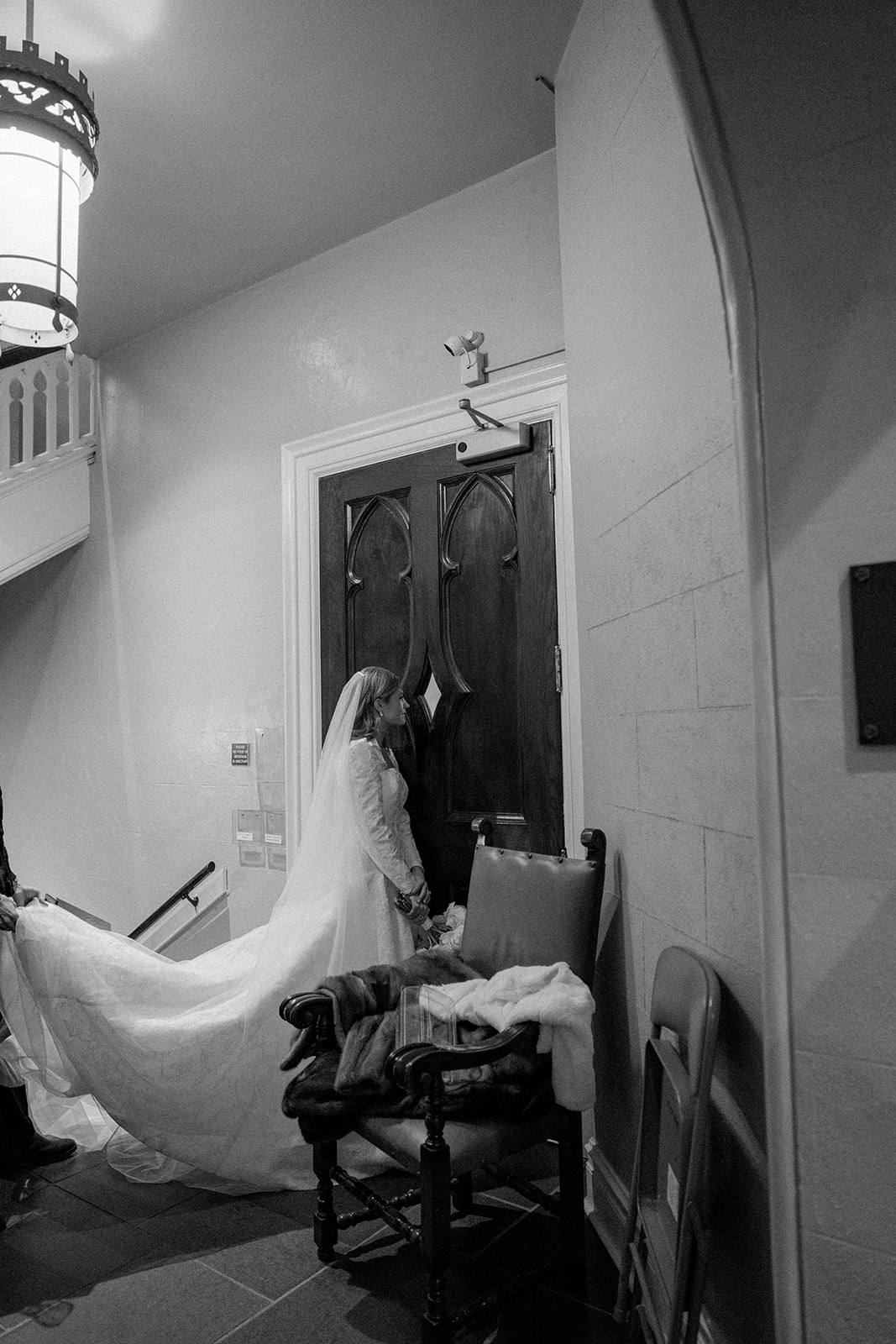 Bride and her dad peak through the window at wedding guests waiting for church ceremony. 