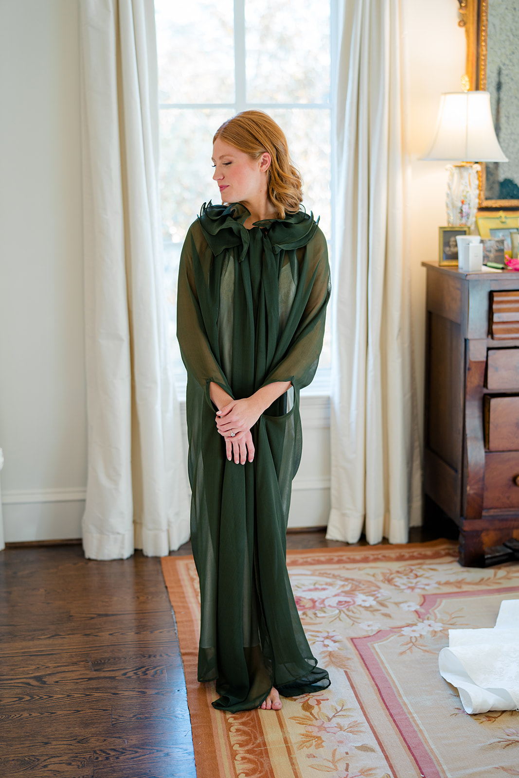 bride standing in dark green robe on the morning of wedding.