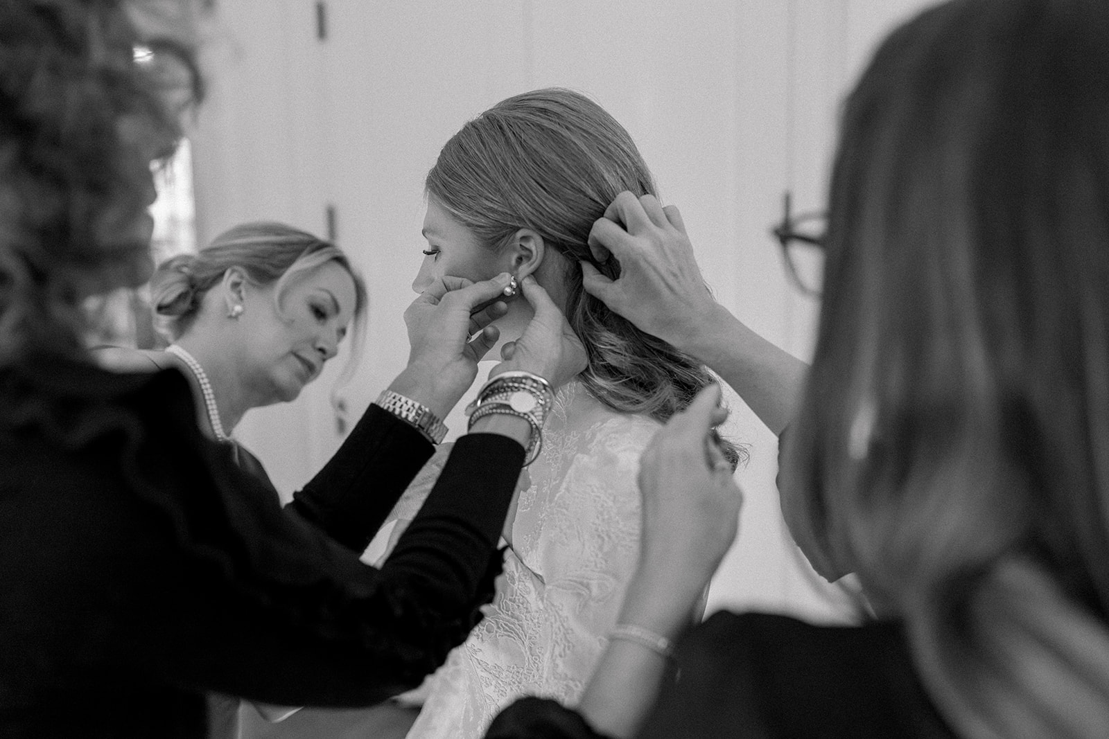 black and white photo of multiple hands reaching to adjusting earrings and hair on bride