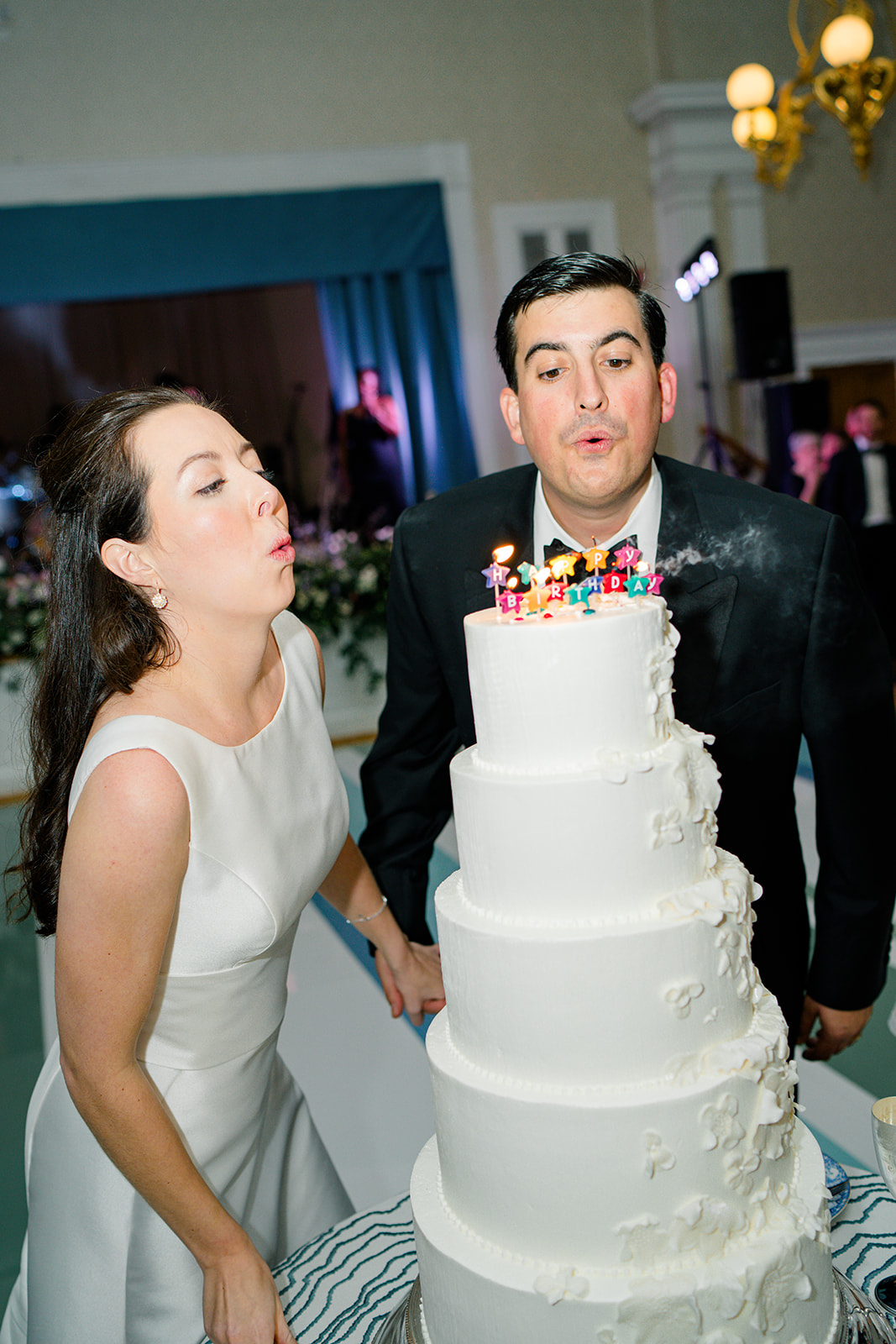 Bride and groom blow out candles on wedding cake for bride's birthday 
