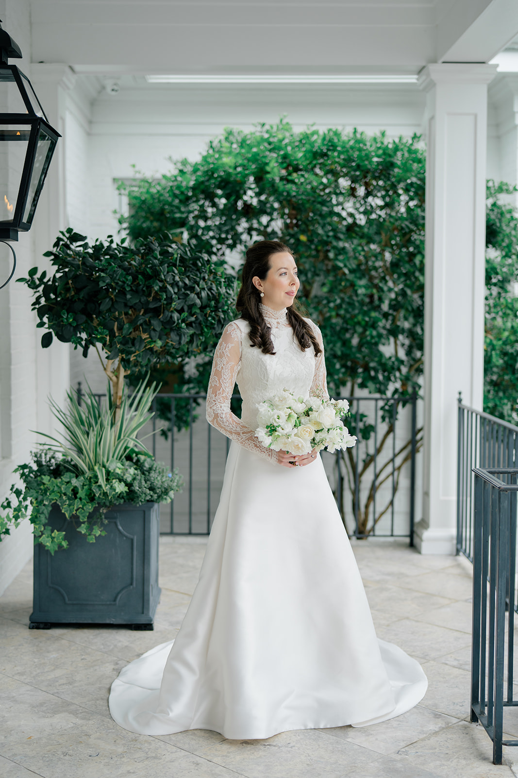 Bride lace sleeve dress with high frill neckline standing on porch with tree in background. 