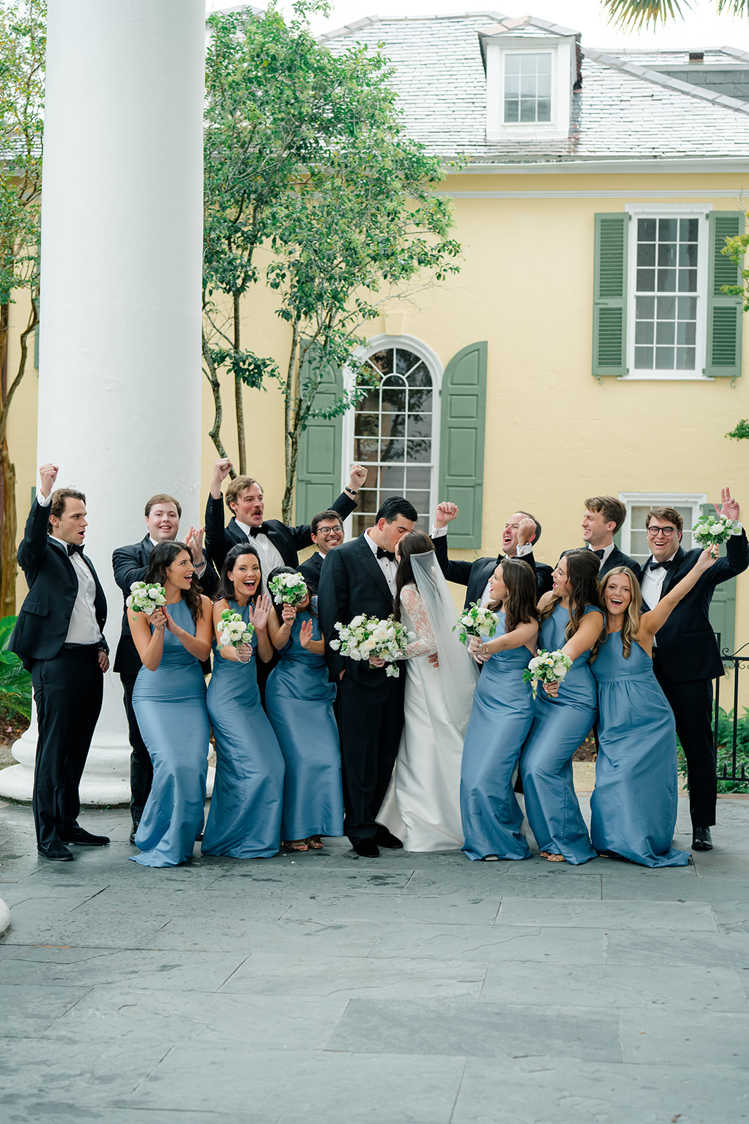 Full bridal party celebrating while bride and groom kiss. 