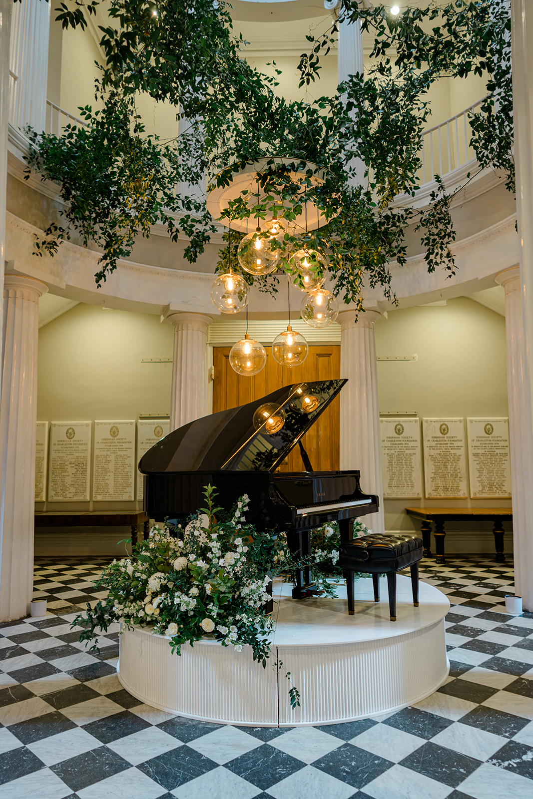 Grand piano on a stage in the rotunda at Hibernian Hall with greenery and lights hanging. 