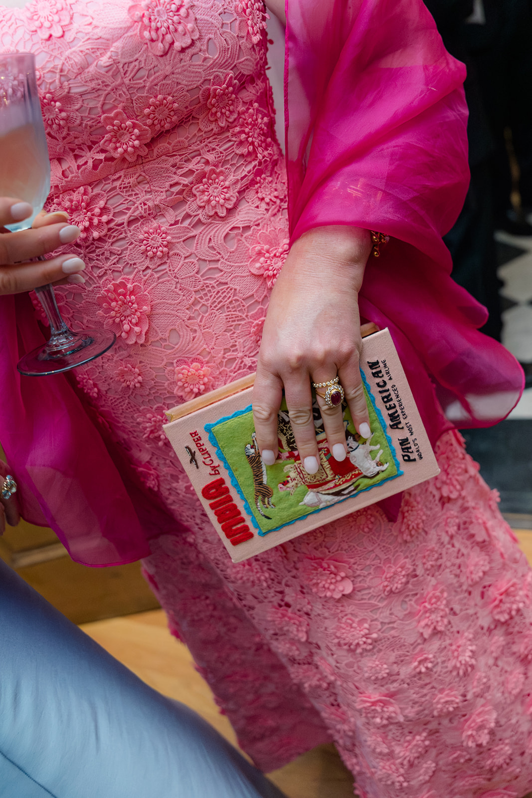 Wedding guest in pink dress holding a book during cocktail hour. 