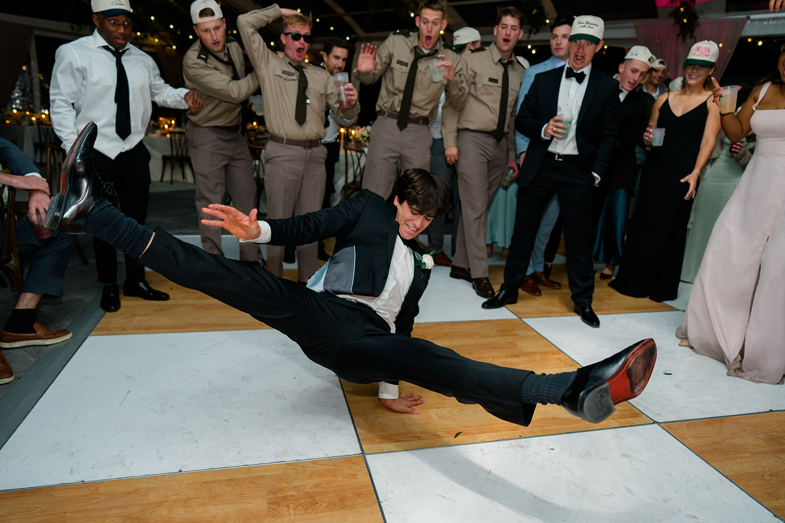 Brother of the bride breakdances during wedding reception. Crowd in background wearing army uniform reacts. 