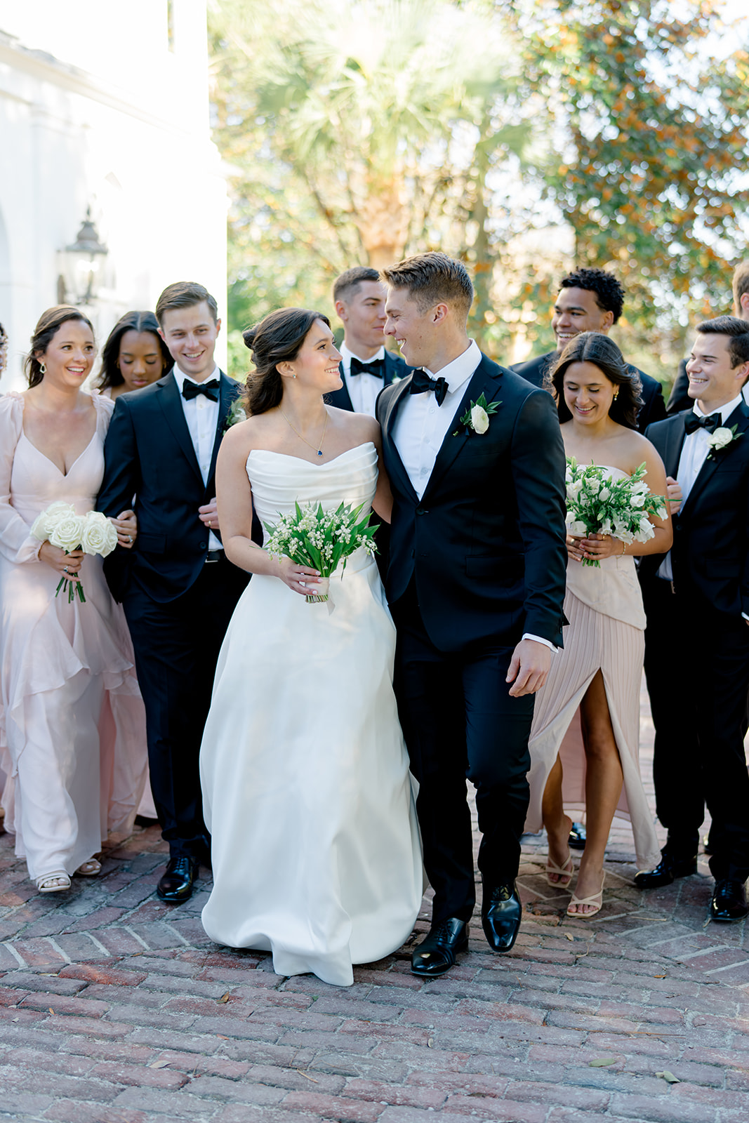 Full bridal party walking together with bride and groom in front of Lowndes Grove house. 