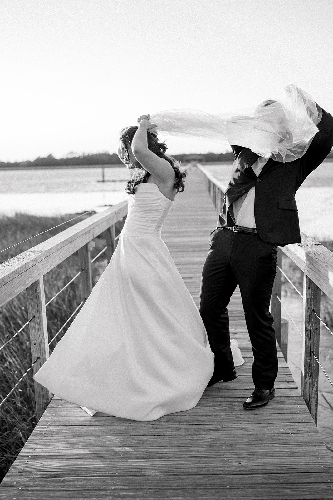 candid photo of groom helping bride with her veil on the dock at Lowndes Grove. 
