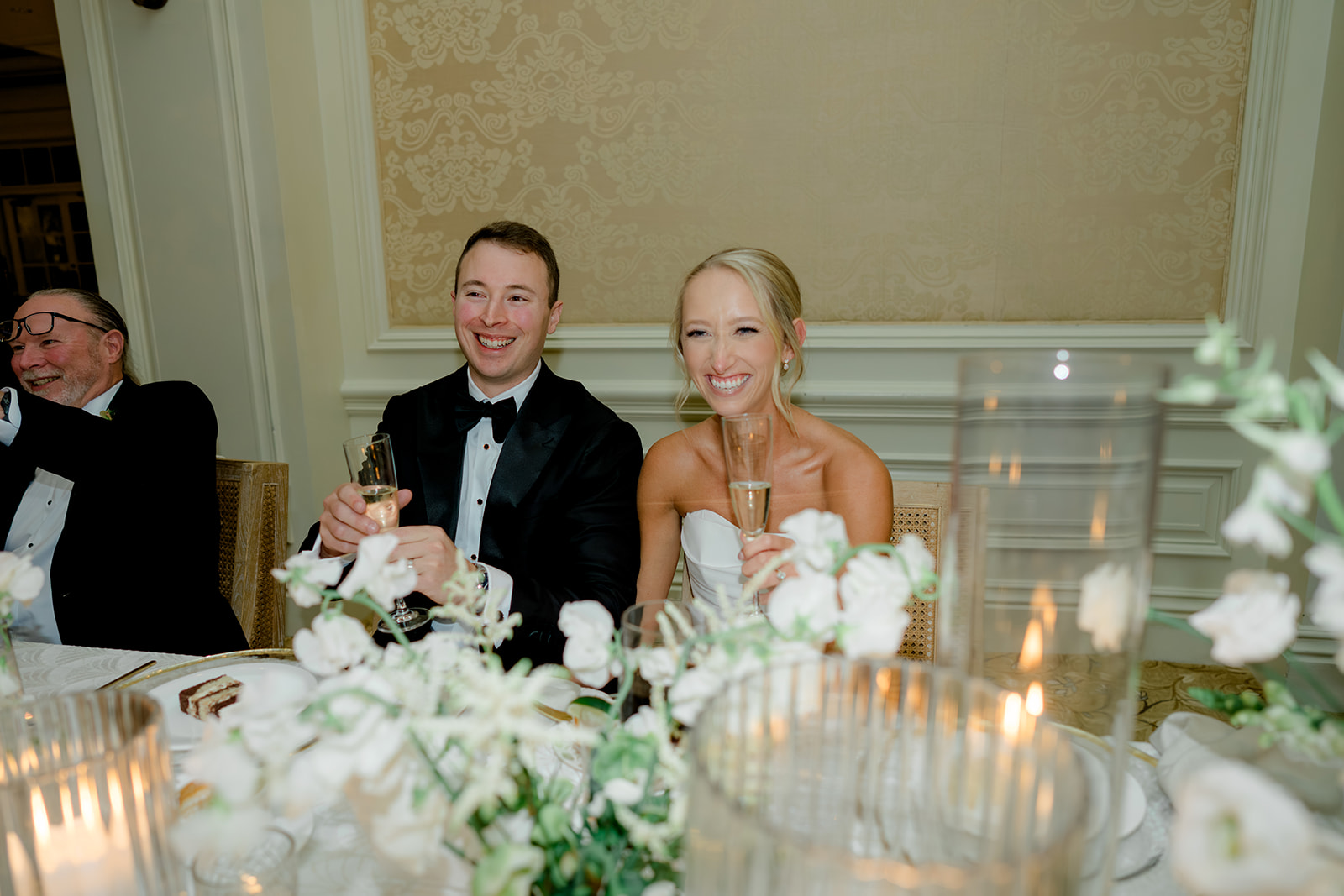 Bride and groom laugh during best man speech. 