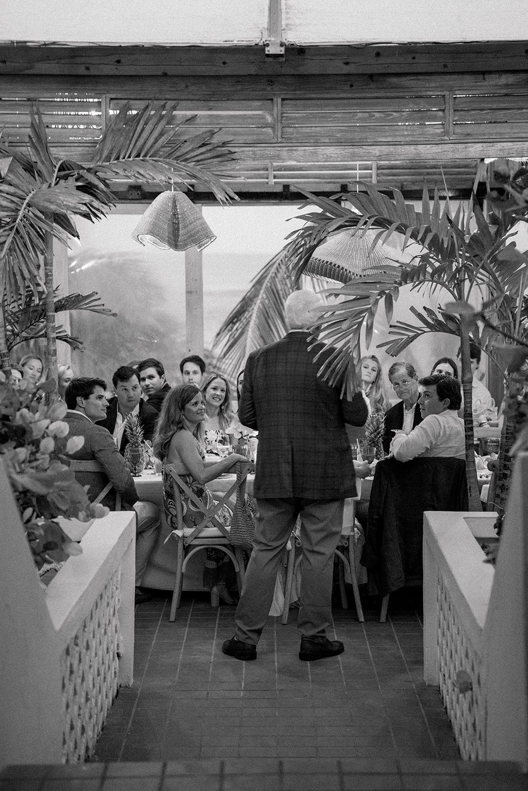 Rehearsal dinner guests watch father of the groom give speech. 