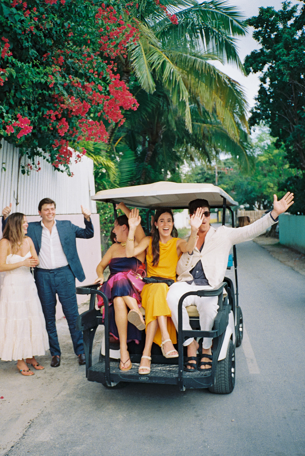 Wedding guests in a golf cart stop for a photo with bride and groom before wedding rehearsal dinner. 