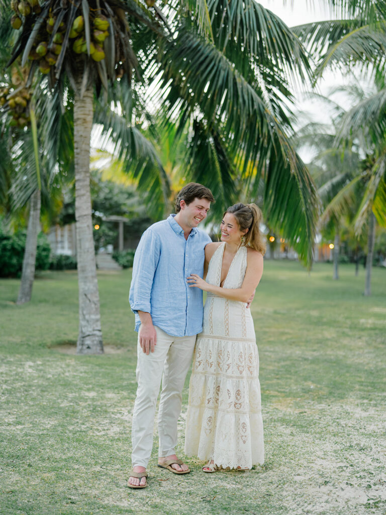 Bride and groom laugh together in front of palm trees. Bahamas welcome dinner at the farm. 
