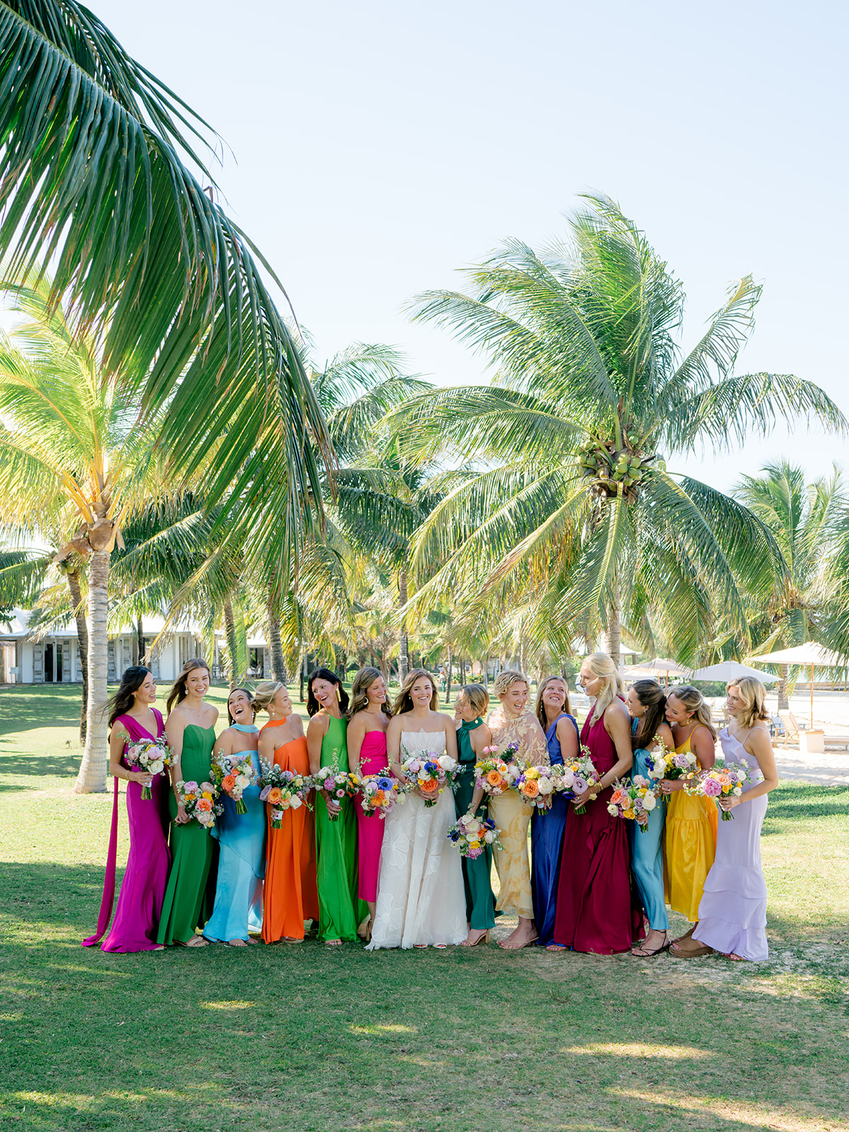Bride and bridesmaids group photo. Bridesmaids in mixmatched bright colored dresses on the lawn at The Otherside Hotel with palm trees in background. 
