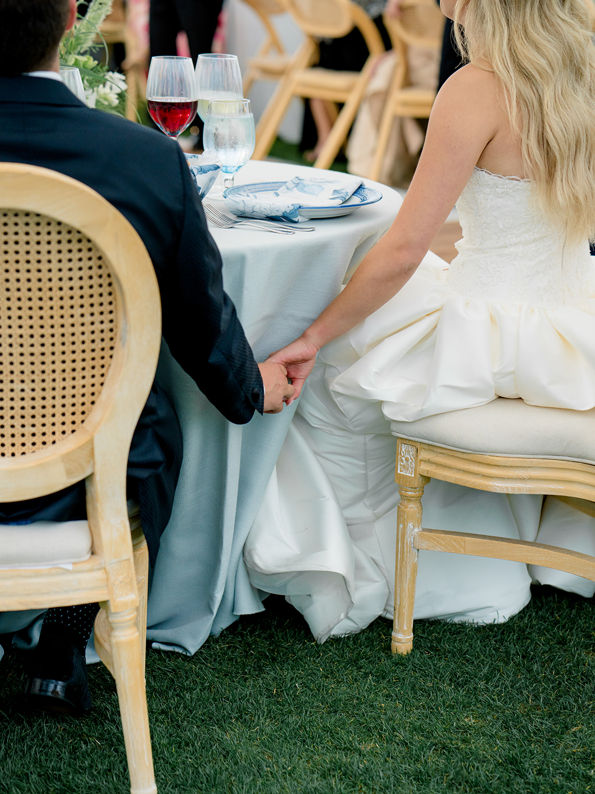 Bride and groom hold hands under the table. Blue and white destination wedding. 
