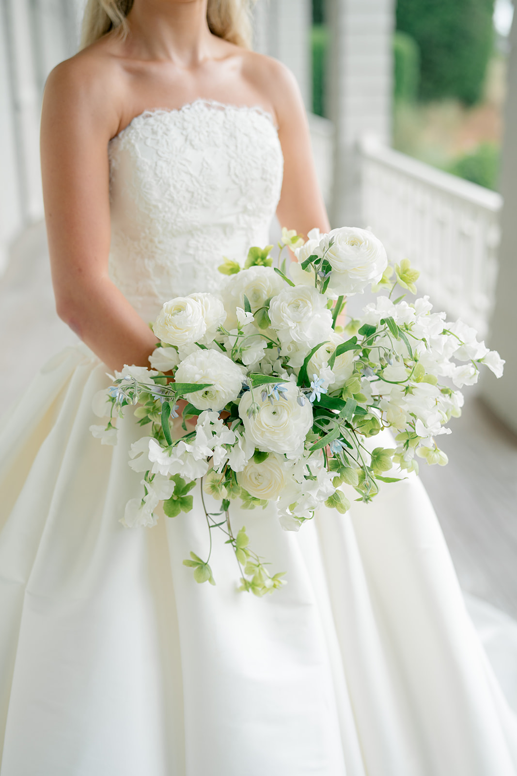 Close up of bride in strapless dress holding white and green flowers. 