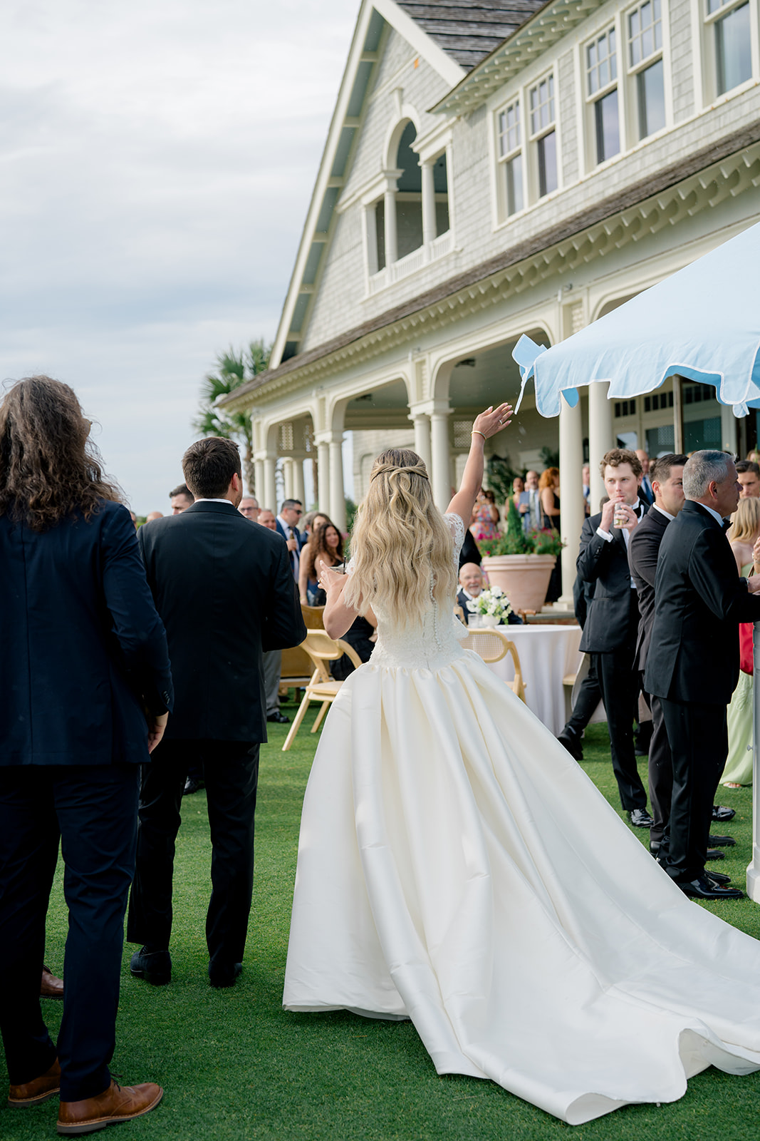 Bride and groom arrive at cocktail hour. Bride waves to her guests. blue umbrella. ocean course cocktail hour