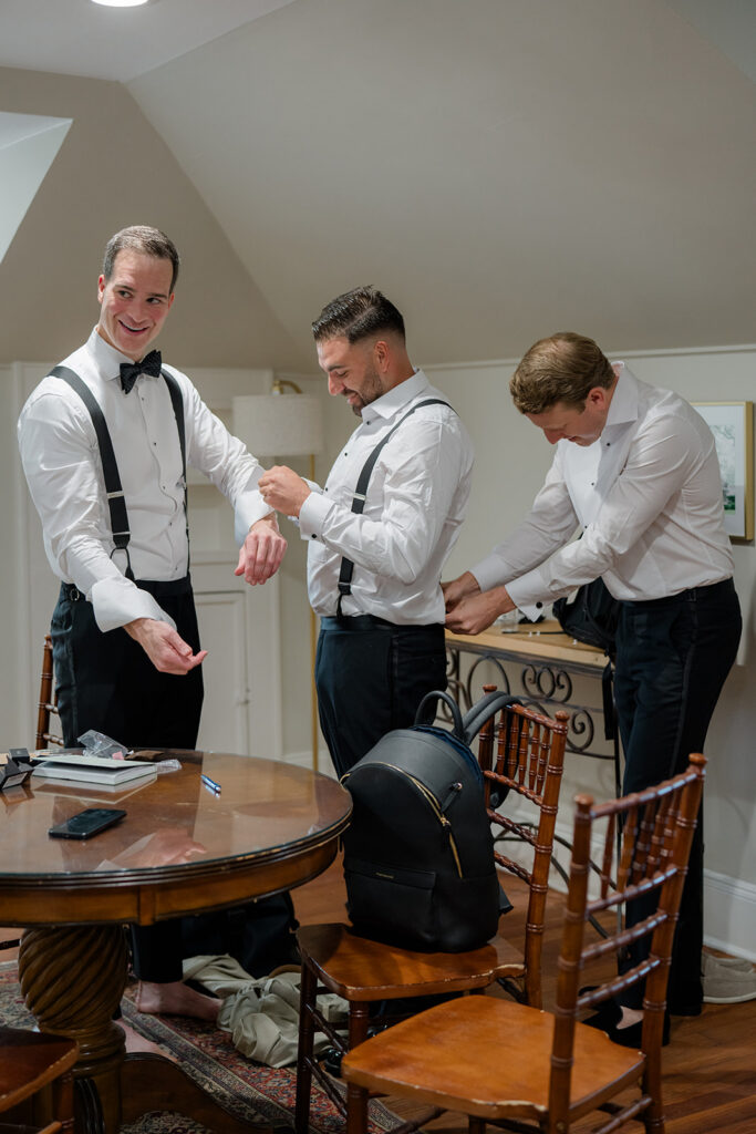 Groomsmen help the groom get dressed on wedding day. 