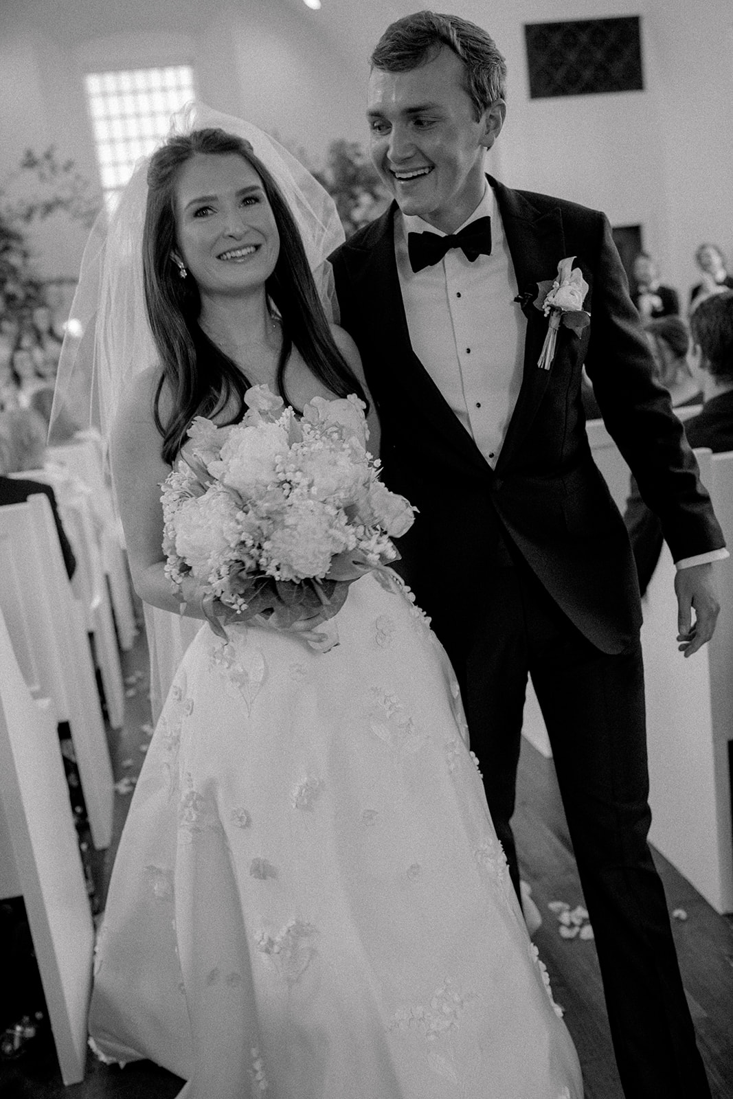 Black and white photo of bride and groom smiling during ceremony exit