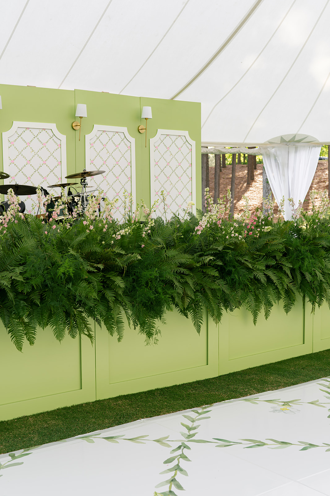 Stage decorated with greenery and green wall with wallpaper and lamps.